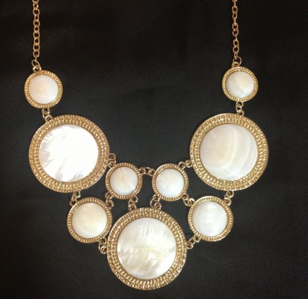 Maxi colar dourado com círculos brancos.